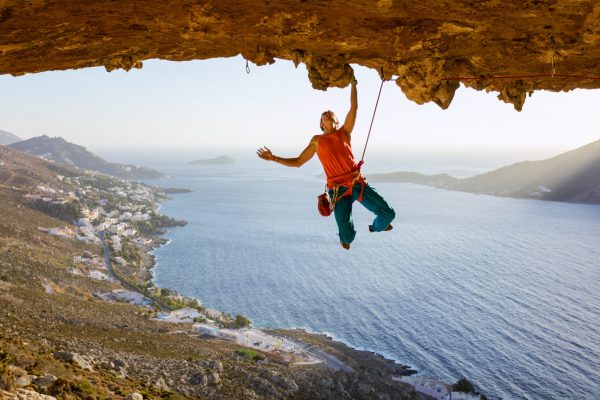 Male rock climber on challenging route going along ceiling in cave, Kalymnos, Greece